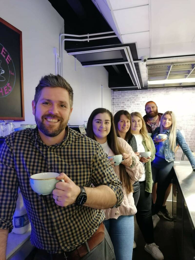 SRC Innovation Skills team are standing in a row in a coffee shop setting, holding coffee cups and smiling. The group is a mixture of male and female.