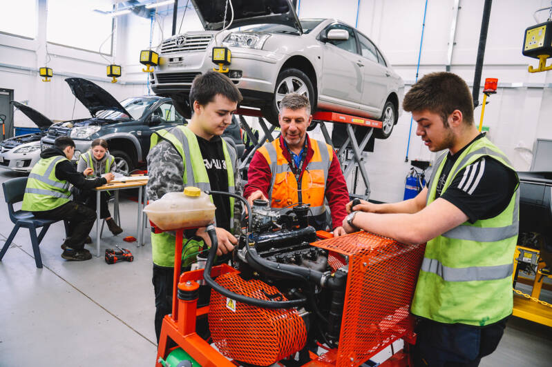 Students and staff wearing hi-vis jackets and working in car maintenance workshop