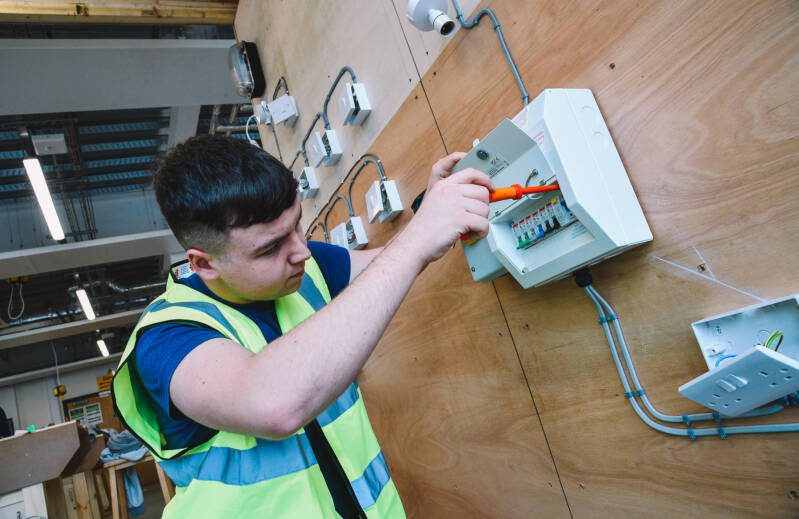 Student wearing hi-vis jacket and protective glasses is working with an electrical consumer unit