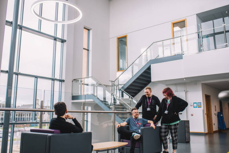 A group of students are smiling and chatting in a bright and modern hallway seating area within the SRC campus.