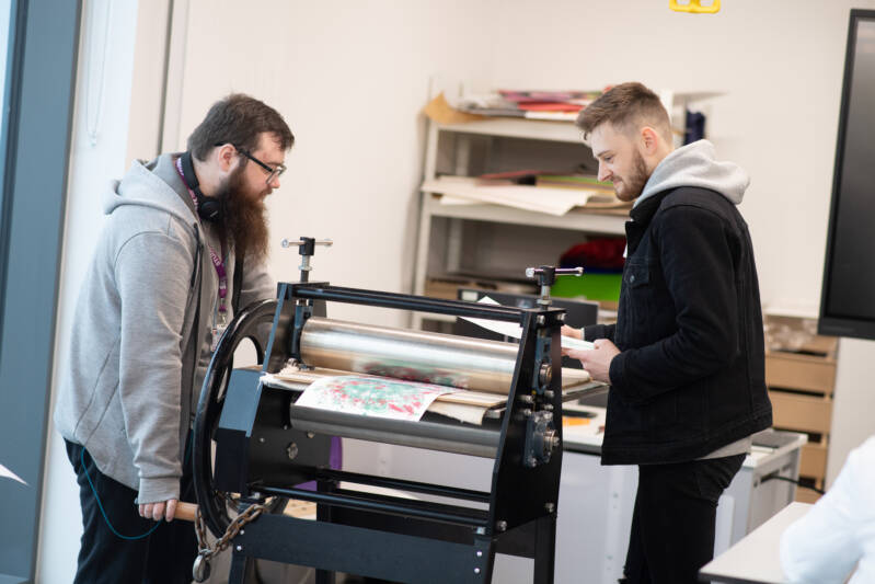 Two male SRC students are using a printing press in an art studio