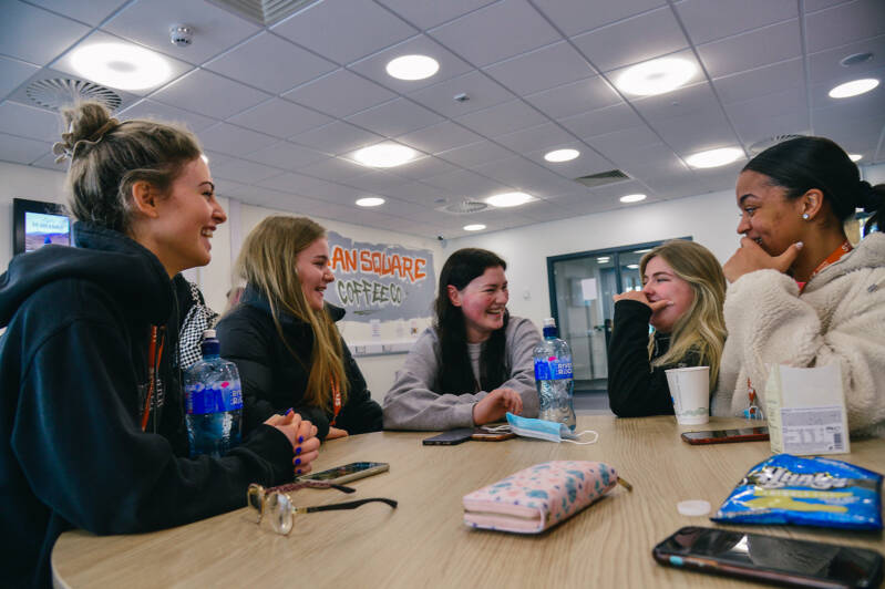 Group of female students smiling and chatting at cafe table