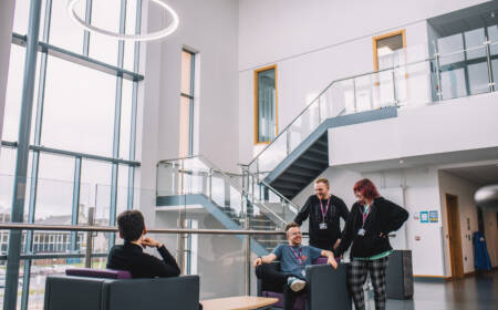 A group of students are smiling and chatting in a bright and modern hallway seating area within the SRC campus.