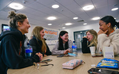 Group of female students smiling and chatting at cafe table