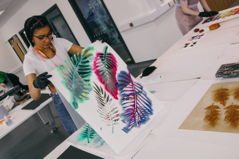An SRC student is creating a piece of artwork using a stencil of large palm leaves.