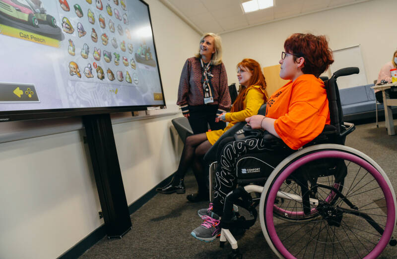 Two SRC students and a member of SRC staff looking at a large interactive whiteboard. One of the students is a wheelchair user.