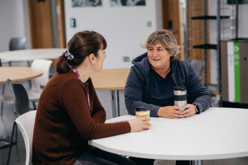 Two female mature students chatting at cafe table