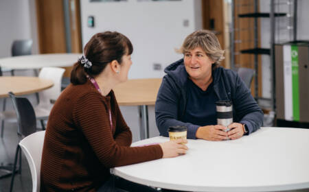 Two female mature students chatting at cafe table